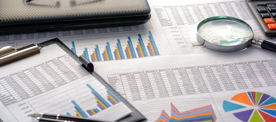 Finanzdokumente - Grafiken, Statistiken, Zeichnungen, Tastatur, Laptop, Lupe im Büro.